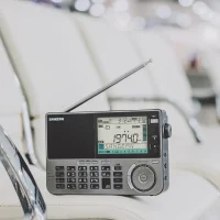 An ATS-909X2 world-band radio receiver with telescopic antenna sitting white leather furniture